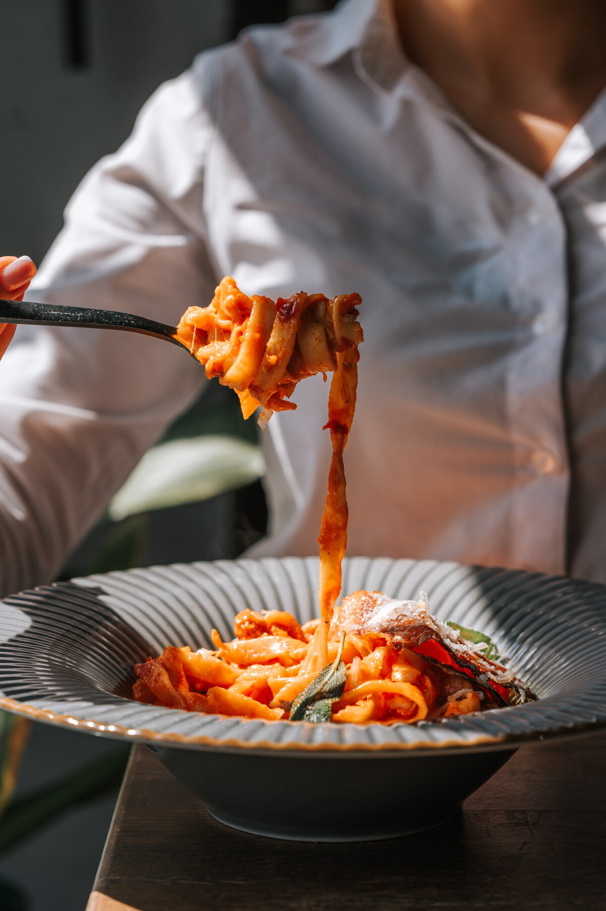 Dłonie kręcą pappardelle w sosie pomidorowym z parmezanem — gość przy stole